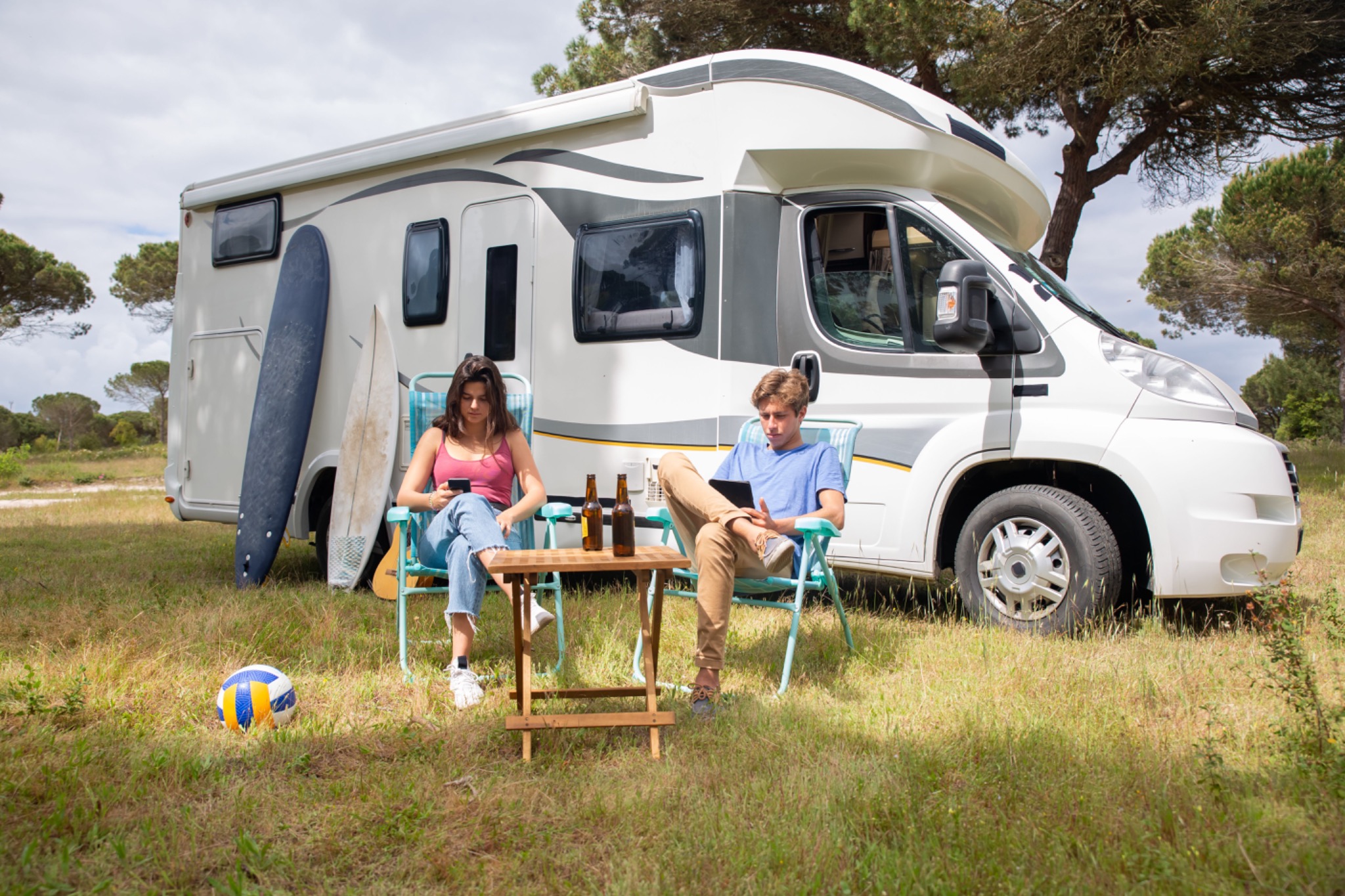 Casal a relaxar junto a uma autocaravana branca num cenário natural em Portugal